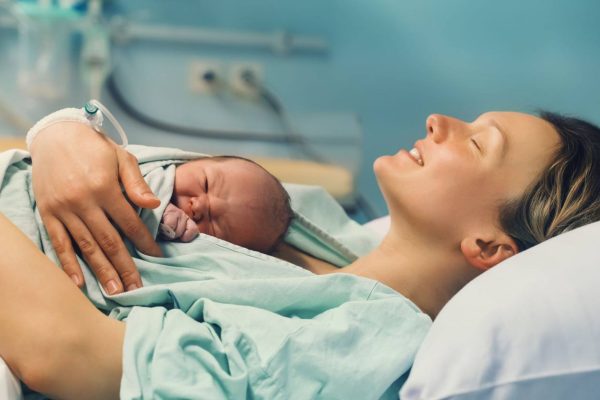 New mother laying down in a hospital bed holding new baby with such joy on her face after giving birth