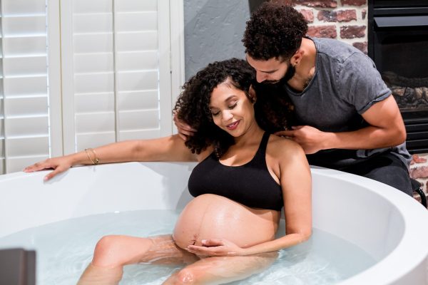 Woman in labor in a birthing tub with her husband next to her rubbing her shoulder and offering her support during birth
