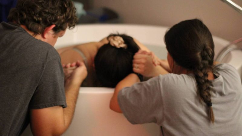 Pregnant woman in a birthing tub holding hands with her two support persons. 