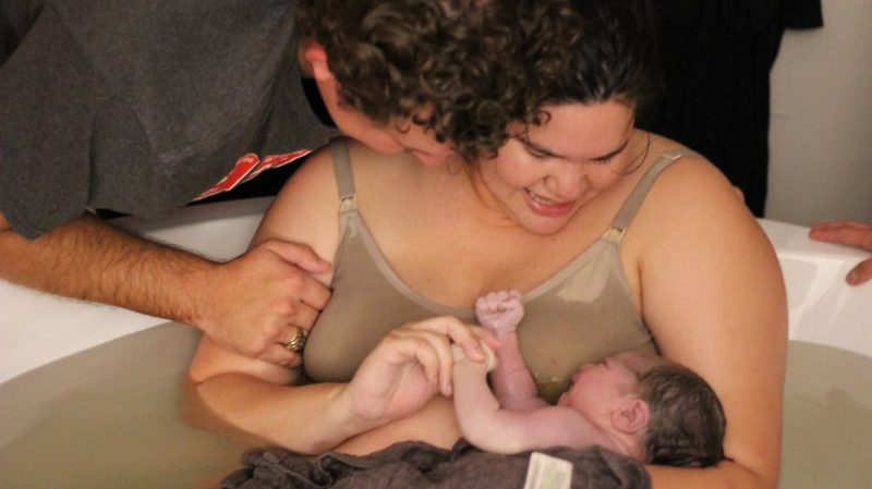 Women in a birth tub holding her newborn baby