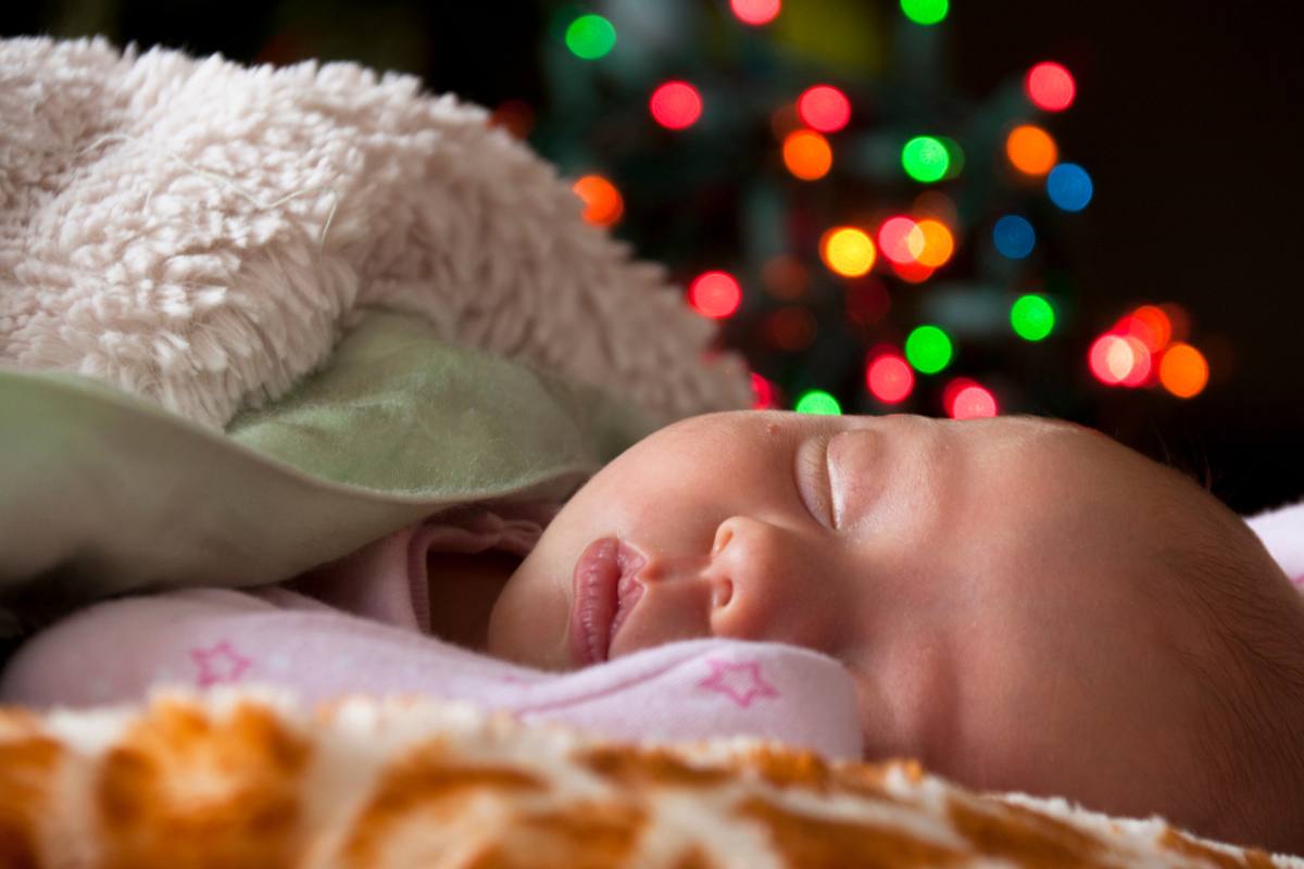 Newborn laying down all swaddled with blankets with bright colorful Christmas lights in the background