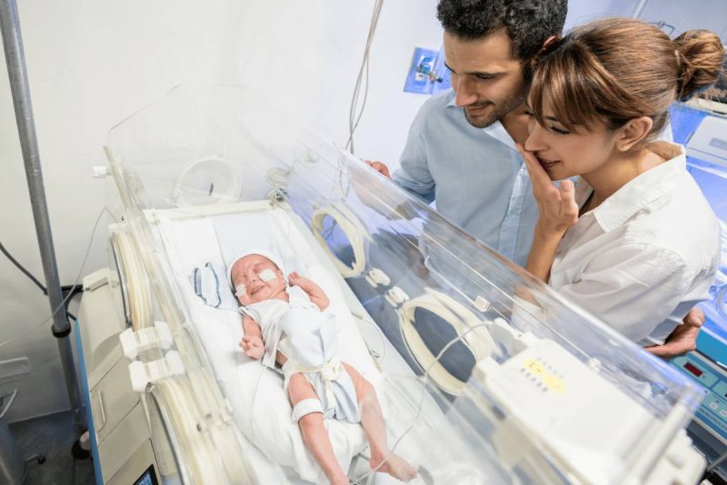 Couple gazes into an incubator which holds their NICU baby. 